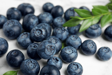 Pile of tasty fresh blueberries and leaves on light table, closeup