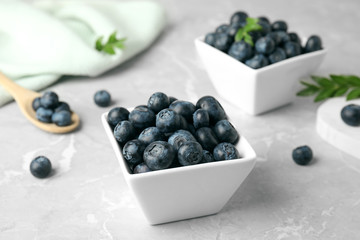 Bowls of tasty blueberries and spoon on grey marble table