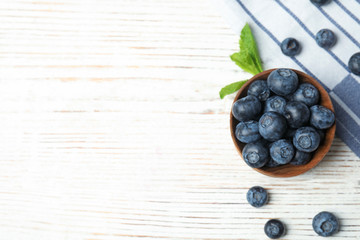 Bowl of tasty blueberries, leaves and fabric on white wooden table, flat lay with space for text