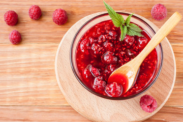 Glass small saucer with raspberry jam with fresh raspberries and mint close-up on wooden background.Copy space