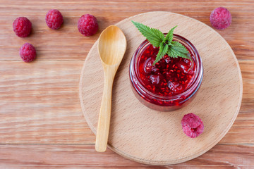 Glass small saucer with raspberry jam with fresh raspberries and mint close-up on wooden background.Copy space