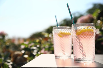 Glasses of pink rose lemonade on  table in blooming garden. Space for text
