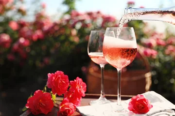 Tragetasche Wein in Glas auf dem Tisch im blühenden Rosengarten gießen. Platz für Text © New Africa