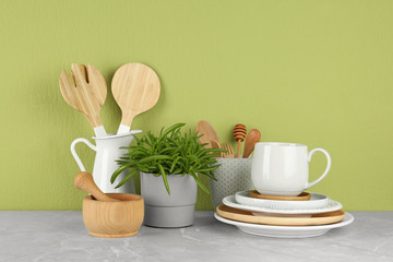 Green plant and different kitchenware on table near color wall. Modern interior design
