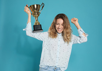 Portrait of happy young woman with gold trophy cup on blue background