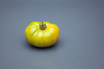 Tomate verde sobre fondo liso, tomate ecológico recién cogido de la mata, tomate verde para que madure fuera de la planta