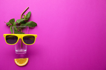 Creative image of summer cocktail made with mint, glass, sunglasses, citrus slice and straw on color background, flat lay. Space for text
