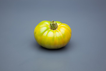 Tomate verde sobre fondo liso, tomate ecológico recién cogido de la mata, tomate verde para que madure fuera de la planta