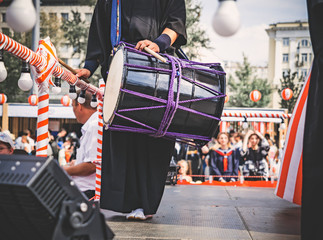 A male Japanese musician, a drummer standing on the stage Yagura is dressed in traditional Japanese black kimono and holds a taiko drum - ready to performance