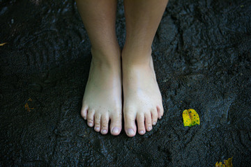 Feet in the dark sand with yellow leaf
