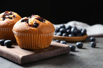Wooden board with blueberry muffins on grey table against black background, closeup view. Space for text
