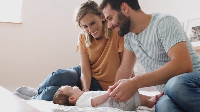 Loving Parents With Newborn Baby Lying On Bed At Home In Loft Apartment