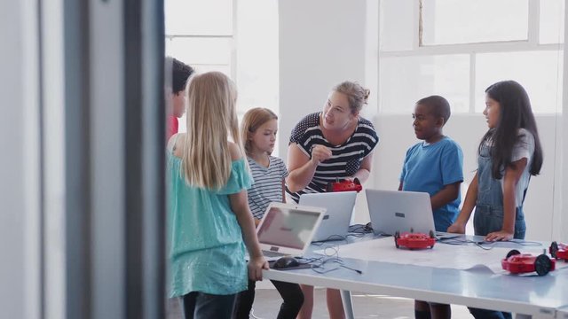 Students With Female Teacher In After School Computer Coding Class Learning To Program Robot Vehicle
