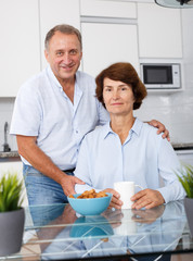Mature family couple sitting together at kitchen table and drinking tea