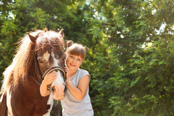 Cute little girl with her pony in green park