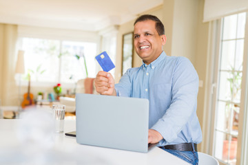 Middle age man showing credit card while using laptop