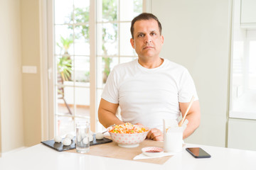Middle age man eating asian food with chopsticks at home with serious expression on face. Simple and natural looking at the camera.