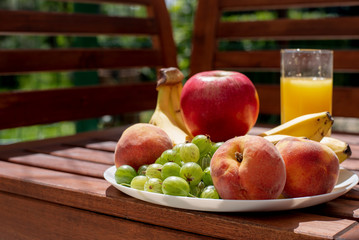 Close-up of fruit on a plate and multifruit juice on a wooden table outdoor in sunny day