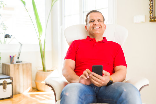 Middle age man smiling cheerful white using smartphone sitting on the sofa at home