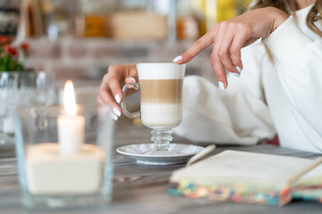 girl holding glass of latte coffee. candle is burning nearby and notepad is lying. Relaxed pastime concept
