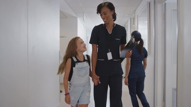 Nurse Walking Holding Hands With Girl Patient In Busy Hospital Corridor