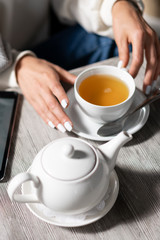 girl in sweater drinking tea in cafe. On table in restaurant is cup of tea and teapot. Cup of tea in hand girl