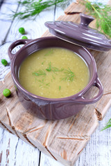 Vegetable pureed soup with asparagus and green peas topped with fresh dill in a ceramic pot