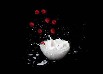 Raspberries falling into milk with a black background. Splashes of milk.