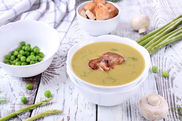 Vegetable pureed soup with asparagus and peas topped with roasted champignons on the white wooden table