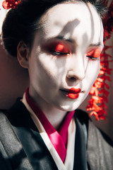 portrait of beautiful geisha with red and white makeup and closed eyes in sunlight with shadows