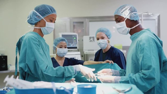 Nurse Hands Surgeon Medical Instruments As Surgical Team Work On Patient In Operating Theatre