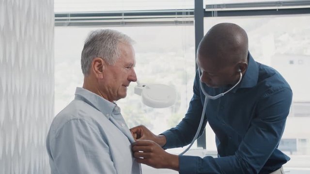 Doctor Listening To Senior Male Patient Breathing With Stethoscope During Medical Exam In Office