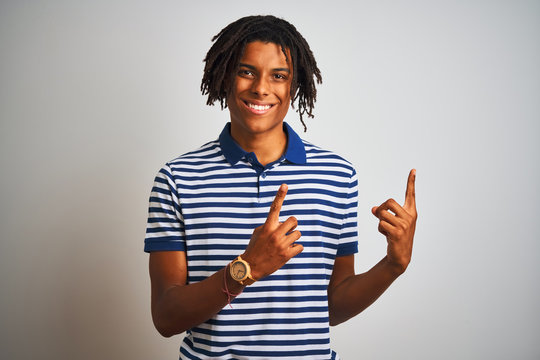 Afro man with dreadlocks wearing striped blue polo standing over isolated white background smiling and looking at the camera pointing with two hands and fingers to the side.