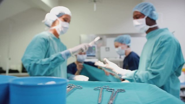 Nurse Hands Surgeon Medical Instruments As Surgical Team Work On Patient In Operating Theatre