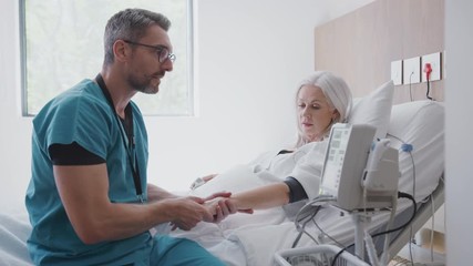 Male Nurse Taking Mature Female Patients Blood Pressure In Hospital Bed With Automated Machine - Powered by Adobe