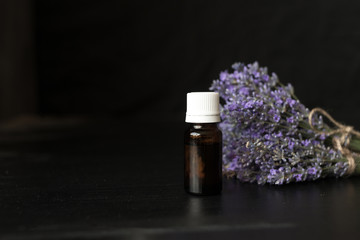 glass bottle with essential oil and fragrant bouquet of lavender flowers on a black background.