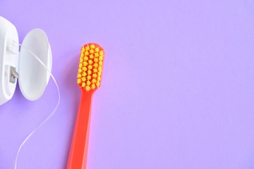 Red plastic toothbrush with yellow bristles and dental floss with selective focus on purple...