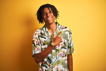 Afro man with dreadlocks on vacation wearing summer shirt over isolated yellow background cheerful with a smile of face pointing with hand and finger up to the side with happy and natural expression 