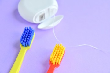 Colorful plastic toothbrushes and dental floss with selective focus on purple background with empty...