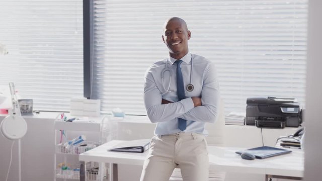 Portrait Of Smiling Male Doctor Sitting On Desk In Office