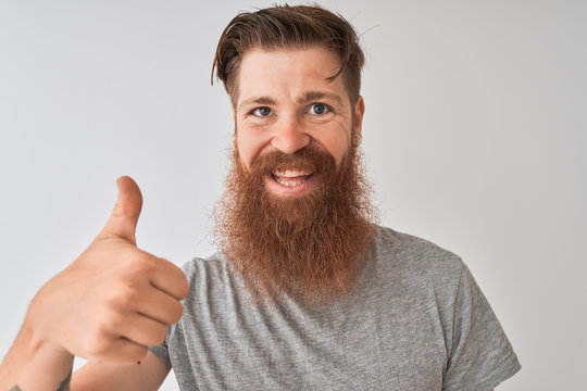 Young redhead irish man wearing t-shirt standing over isolated grey background happy with big smile doing ok sign, thumb up with fingers, excellent sign