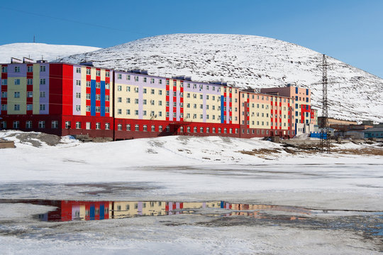 City in the far north in the Arctic. Colorful buildings on the background of snow-capped mountains. The end of May in the Arctic. Pevek is the northernmost city in Russia. Chukotka, Siberia, Russia.