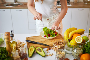 Young happy woman preparing tasty salad in the beautiful kitchen with green fresh ingredients...