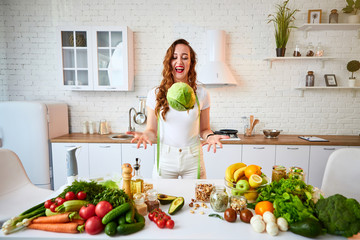 Young happy woman holding cabbage in the beautiful kitchen with green fresh ingredients indoors. Healthy food and Dieting concept. Loosing Weight