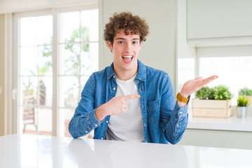 Young handsome man wearing casual denim jacket at home amazed and smiling to the camera while presenting with hand and pointing with finger.