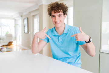 Young handsome man wearing casual blue t-shirt at home looking confident with smile on face,...