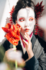 selective focus of sakura branches and beautiful geisha holding red flowers in sunlight