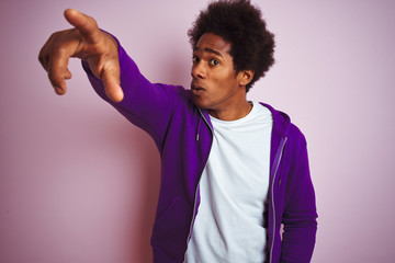 Young african american man wearing purple sweatshirt standing over isolated pink background Pointing with finger surprised ahead, open mouth amazed expression, something on the front