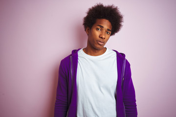 Young african american man wearing purple sweatshirt standing over isolated pink background looking...