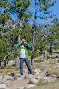 Adult hiker man looking through binoculars in forest at countryside